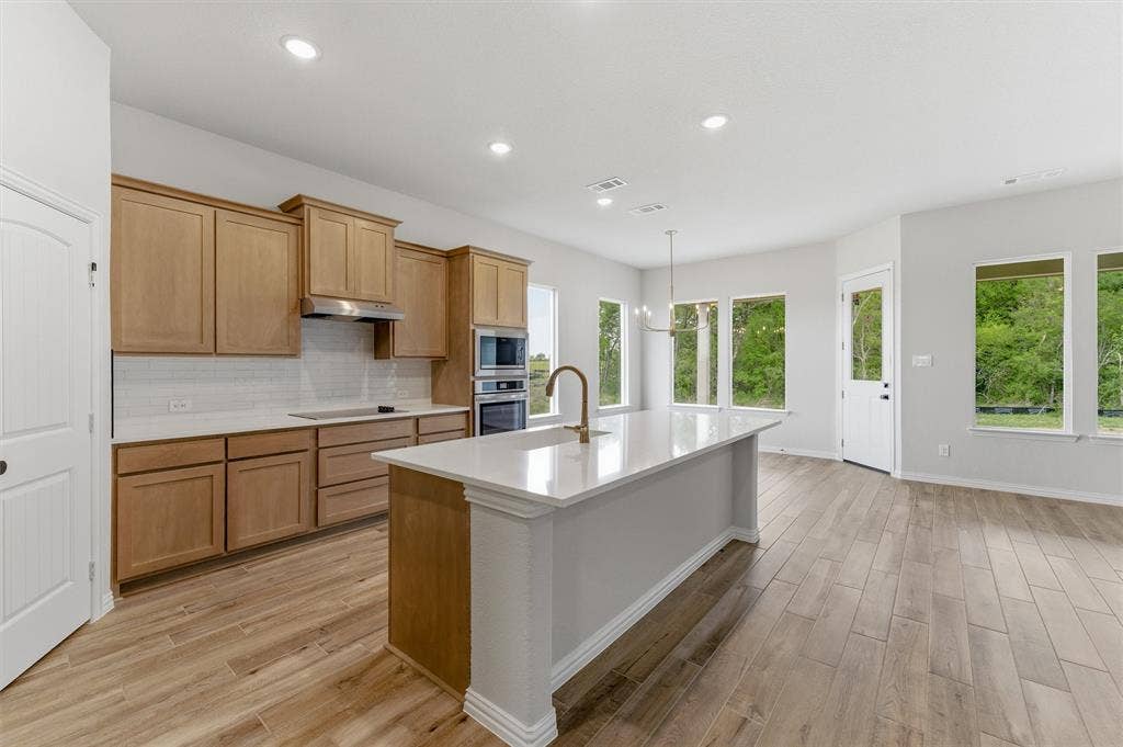 9007 County Road 623, Blue Ridge, TX 75424 Kitchen with light wood-type flooring, a kitchen island with sink, decorative backsplash, stainless steel appliances, and light stone counters