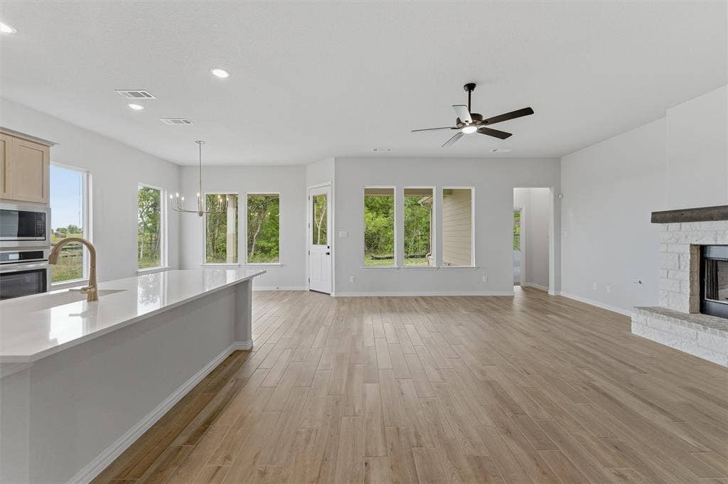 9007 County Road 623, Blue Ridge, TX 75424 Unfurnished living room featuring a fireplace with raised hearth, light wood finished floors, suspended lighting, and a ceiling fan