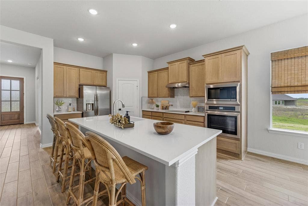 9007 County Road 623, Blue Ridge, TX 75424 Kitchen featuring a large central island with seating, stainless steel appliances, light wood-finish cabinetry, recessed lighting, and wood-finish flooring