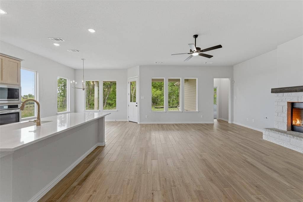 9007 County Road 623, Blue Ridge, TX 75424 Unfurnished living room with a warm lit fireplace, light wood-style floors, healthy amount of natural light, and suspended lighting