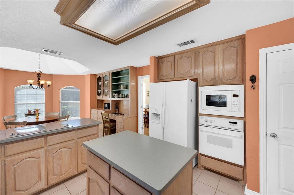 Kitchen featuring glass insert cabinets, white appliances, a chandelier, light tile patterned floors, and a center island