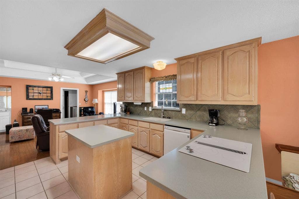 Kitchen with light brown cabinetry, a raised ceiling, a center island, a peninsula, and light tile patterned floors
