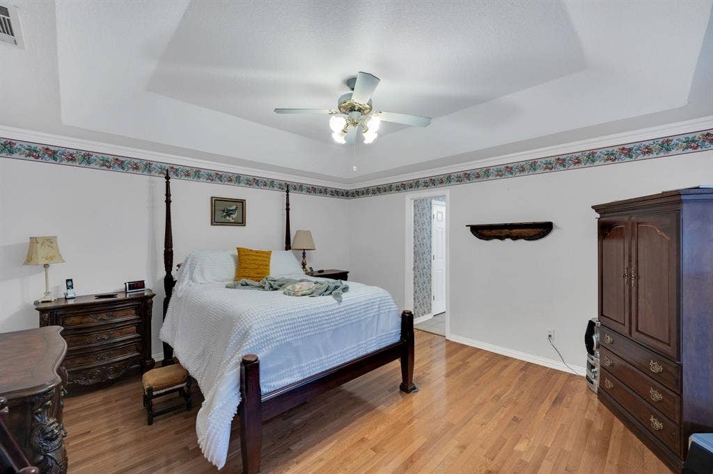 Bedroom with a tray ceiling, light wood finished floors, and ceiling fan
