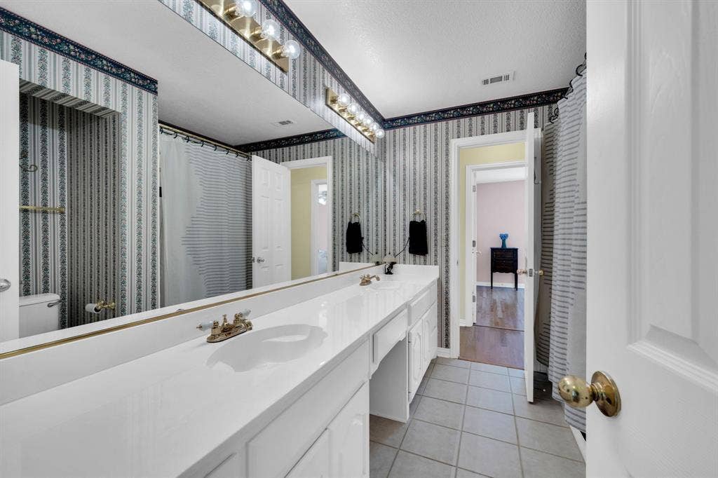 Full bathroom with double vanity, light tile patterned floors, wallpapered walls, and a shower with shower curtain