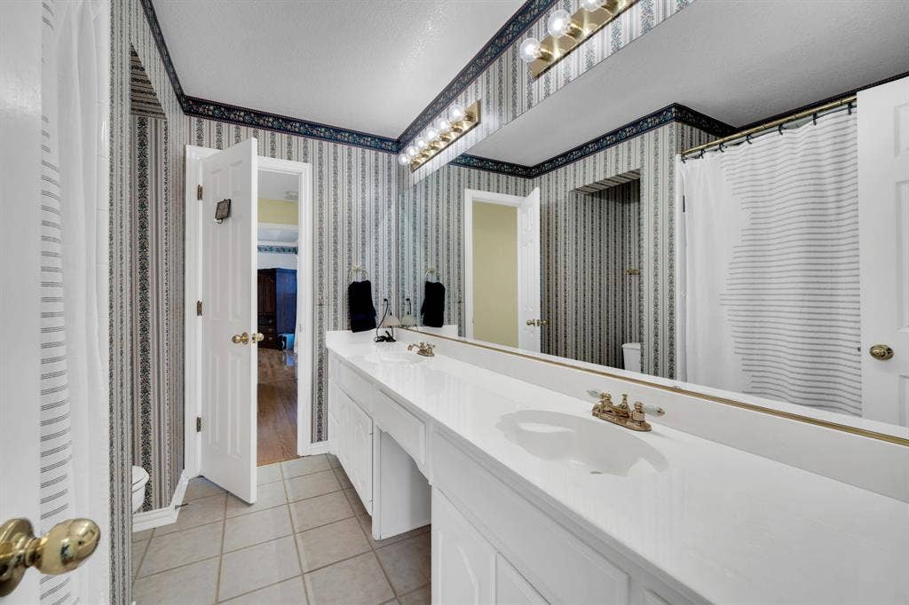Bathroom featuring double vanity, light tile patterned flooring, a shower with shower curtain, and wallpapered walls