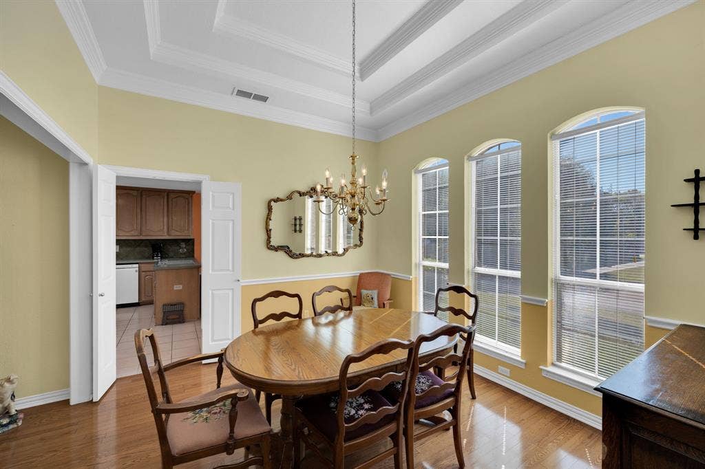 Dining space featuring light wood-style floors, a raised ceiling, a chandelier, and crown molding