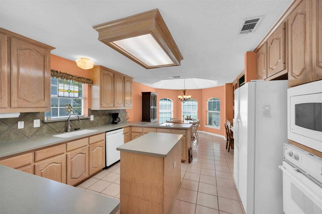Kitchen with light tile patterned floors, white appliances, light brown cabinetry, a kitchen island, and a chandelier