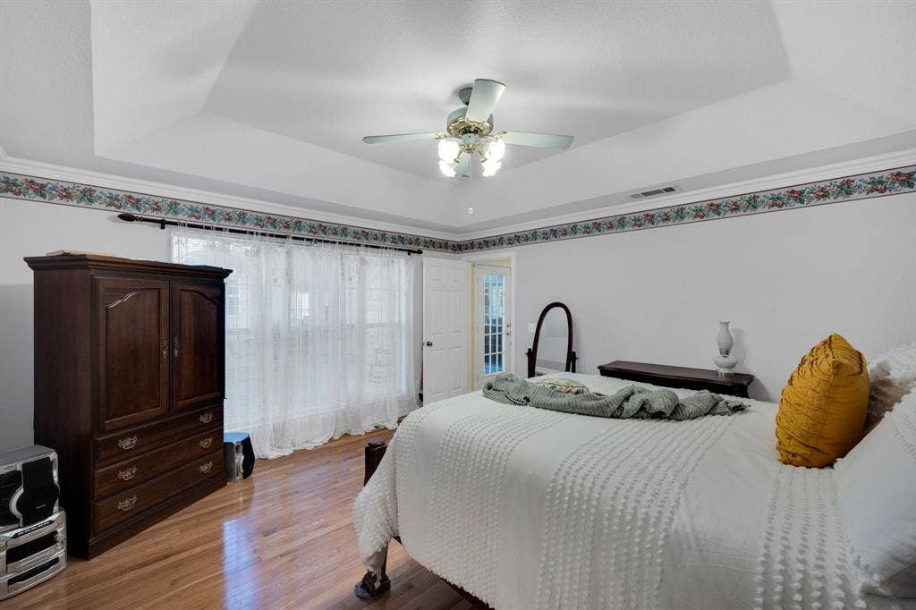 Bedroom with a raised ceiling, light wood finished floors, and ceiling fan