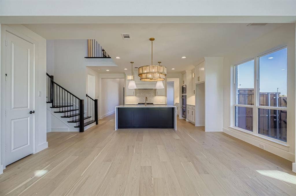 Kitchen featuring white cabinets, pendant lighting, dark cabinets, tasteful backsplash, and a center island with sink