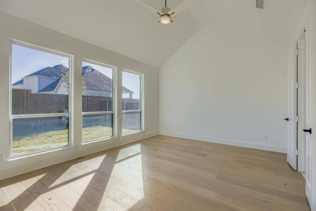 Unfurnished room featuring light wood-type flooring, lofted ceiling, and a ceiling fan