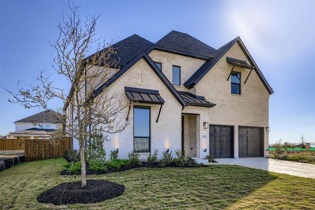 French country home featuring a standing seam roof, brick siding, an attached garage, a metal roof, and driveway