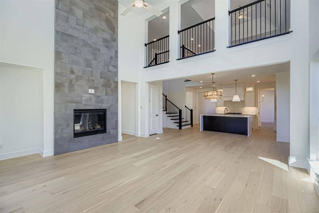 Unfurnished living room featuring a tiled fireplace, light wood-type flooring, a towering ceiling, stairway, and recessed lighting