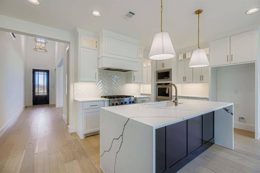 Kitchen with decorative backsplash, decorative light fixtures, light stone countertops, white cabinetry, and recessed lighting