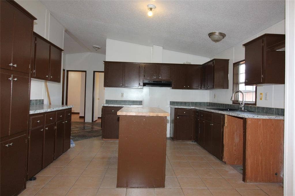 5199 Timarron Drive, Scurry, TX 75158 Kitchen with vaulted ceiling, a kitchen island, light countertops, dark brown cabinets, and light tile patterned floors