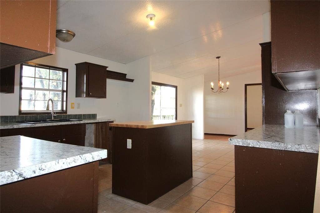 5199 Timarron Drive, Scurry, TX 75158 Kitchen featuring dark brown cabinetry, a kitchen island, light countertops, light tile patterned floors, and pendant lighting