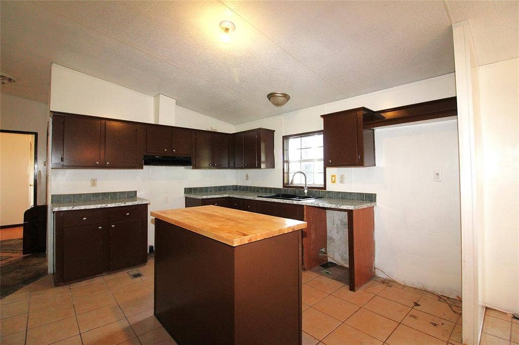 5199 Timarron Drive, Scurry, TX 75158 Kitchen with dark brown cabinetry, wooden counters, vaulted ceiling, light tile patterned flooring, and a kitchen island