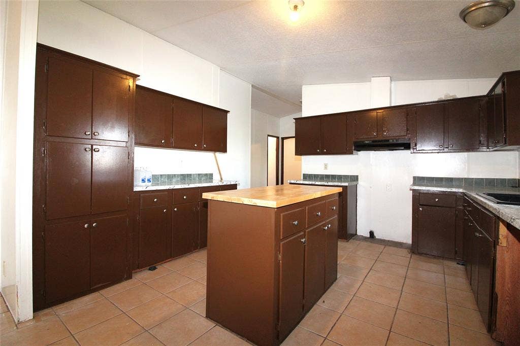 5199 Timarron Drive, Scurry, TX 75158 Kitchen with dark brown cabinetry, light tile patterned flooring, a kitchen island, lofted ceiling, and under cabinet range hood
