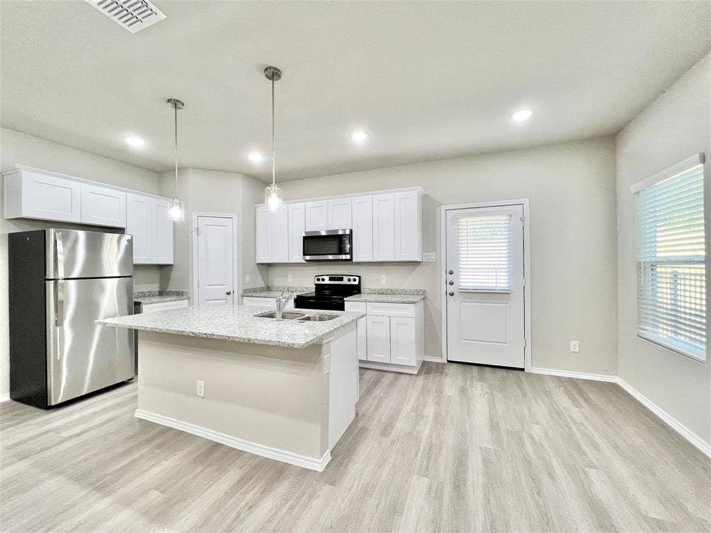 3501 E Renfro Street, #106, Burleson, TX 76028 Kitchen with stainless steel appliances, white cabinetry, light wood finished floors, light stone counters, and a center island with sink
