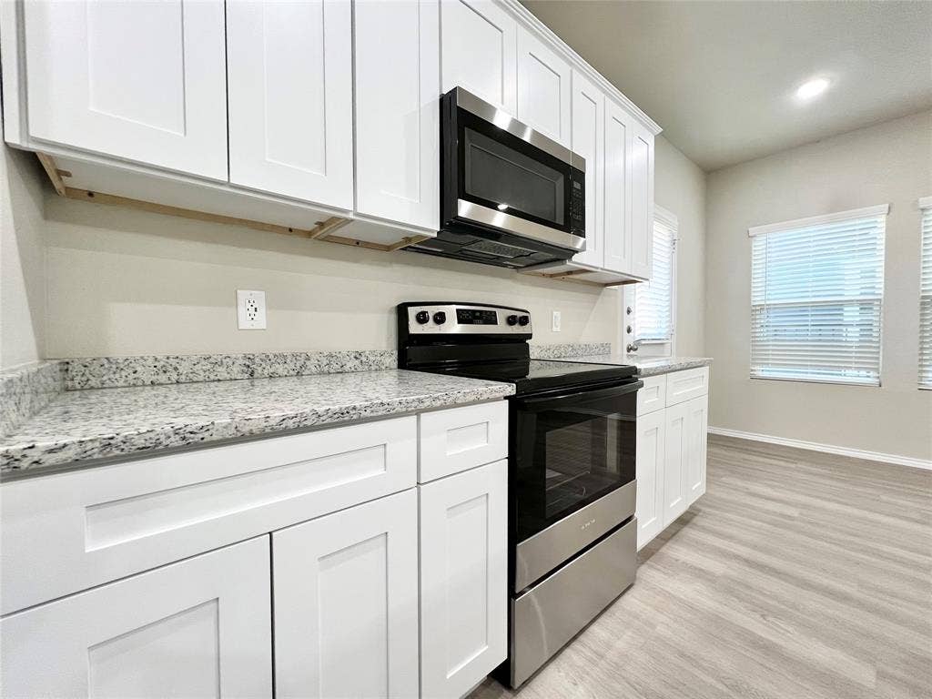 3501 E Renfro Street, #106, Burleson, TX 76028 Kitchen with stainless steel appliances, light wood-type flooring, white cabinetry, light stone countertops, and recessed lighting
