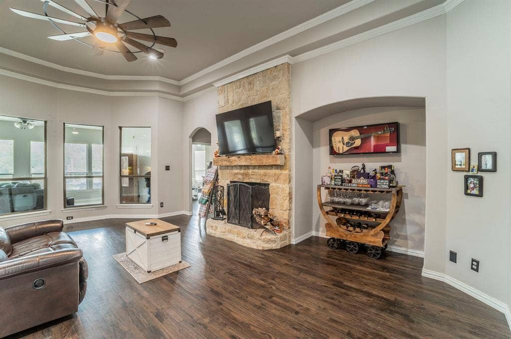 5229 Horseshoe Lane, Royse City, TX 75189 Living room featuring a stone fireplace, crown molding, dark wood-type flooring, ceiling fan, and arched walkways