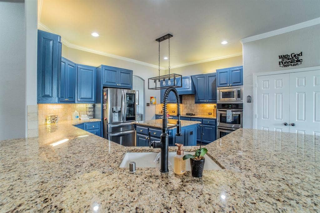 5229 Horseshoe Lane, Royse City, TX 75189 Kitchen with blue cabinets, appliances with stainless steel finishes, decorative backsplash, light stone countertops, and crown molding