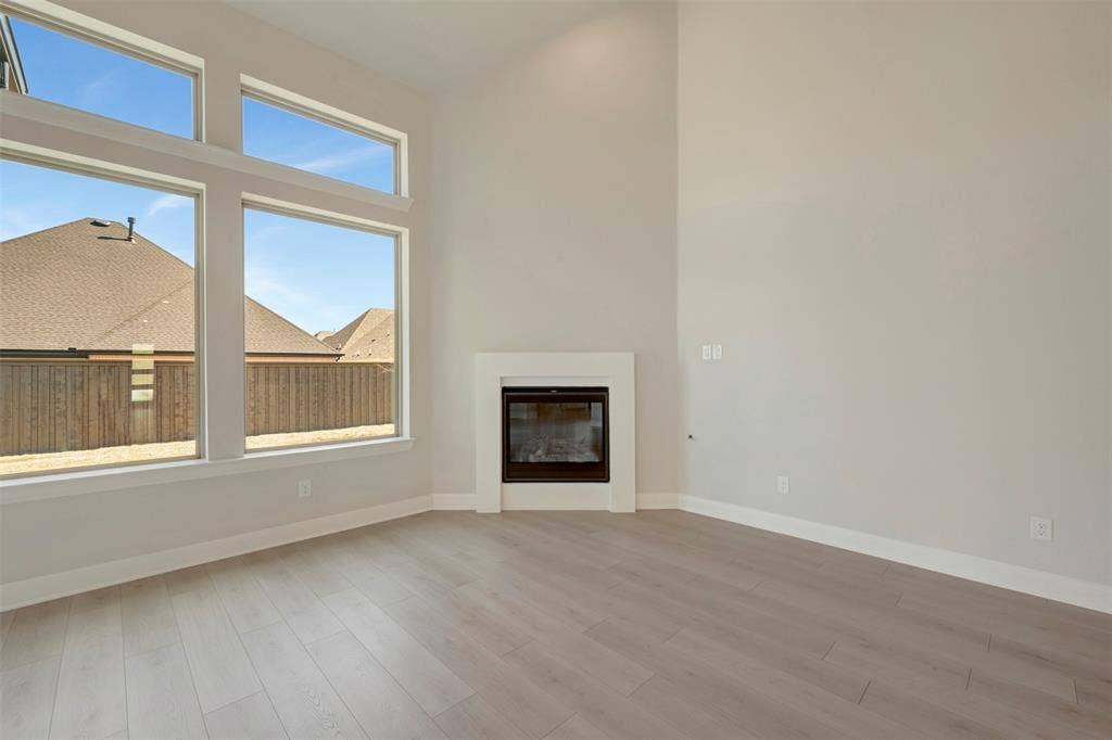 3752 Bermuda Grass Way, Grand Prairie, TX 76084 Unfurnished living room featuring a glass covered fireplace, light wood-style flooring, and a high ceiling