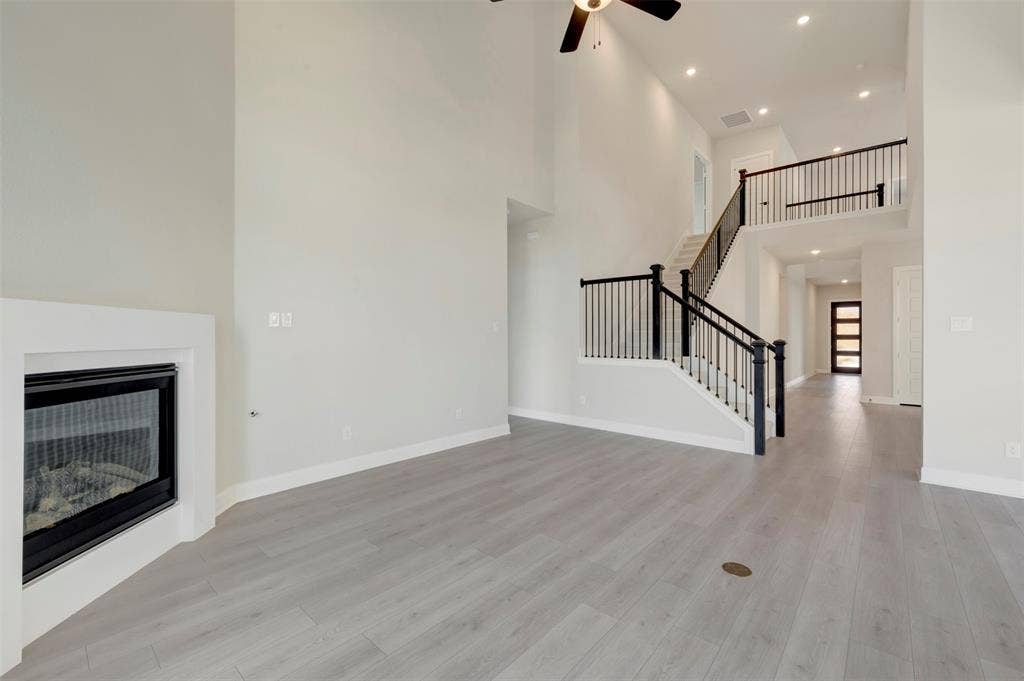 3752 Bermuda Grass Way, Grand Prairie, TX 76084 Unfurnished living room with a glass covered fireplace, ceiling fan, a high ceiling, light wood-type flooring, and recessed lighting
