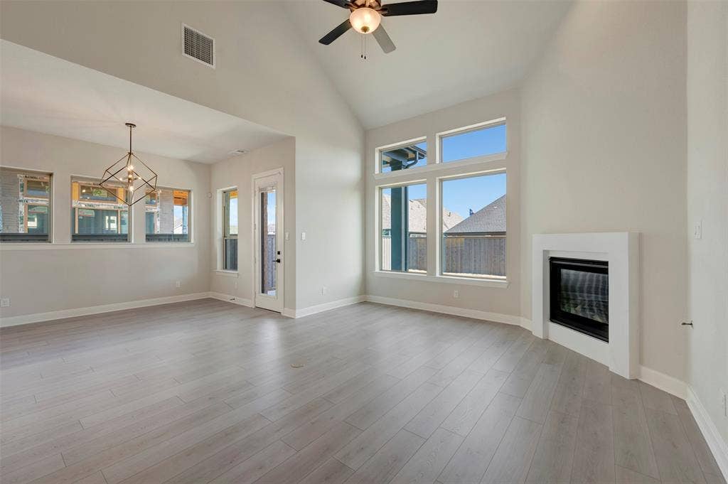 3752 Bermuda Grass Way, Grand Prairie, TX 76084 Unfurnished living room featuring vaulted ceiling, a glass covered fireplace, a ceiling fan, and light wood-type flooring