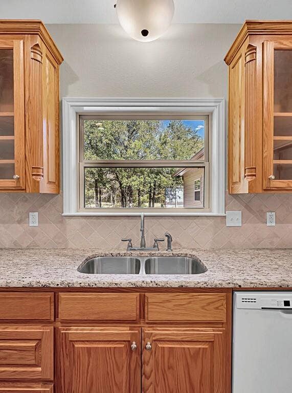 556 Wildwood Trail, Lorena, TX 76655 Kitchen featuring backsplash, glass insert cabinets, dishwasher, light stone countertops, and brown cabinets