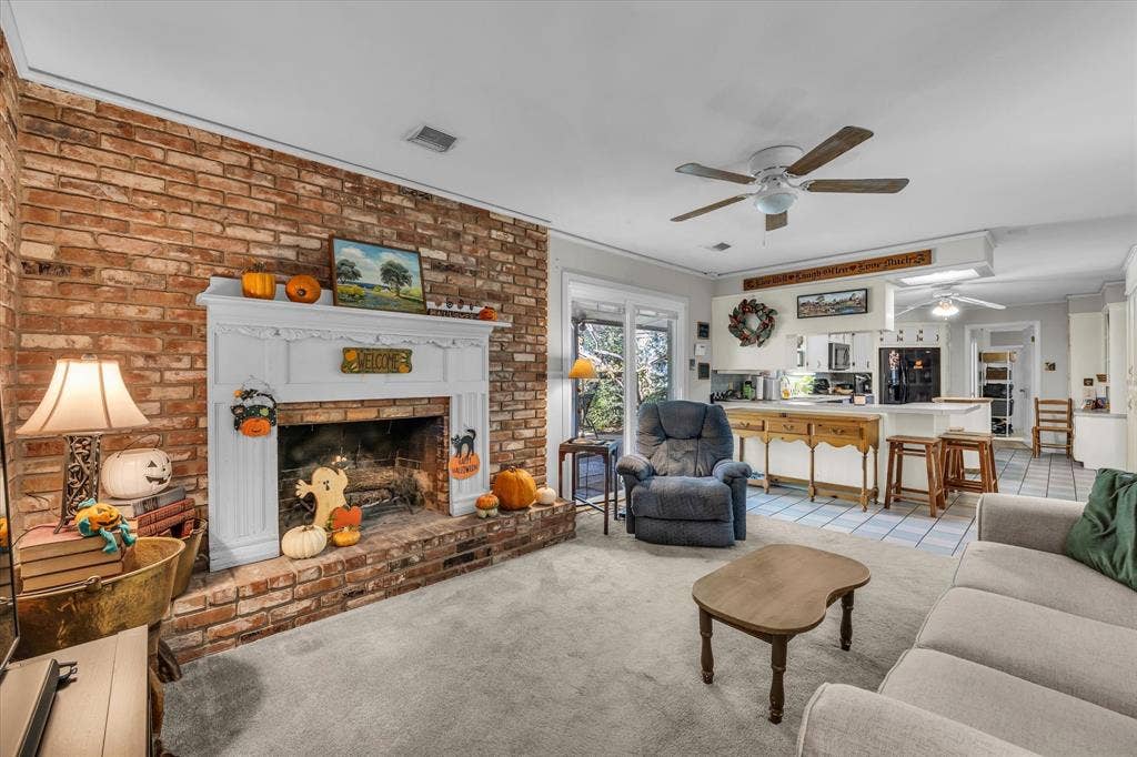 Living area featuring light carpet, a brick fireplace, light tile patterned floors, a ceiling fan, and brick wall