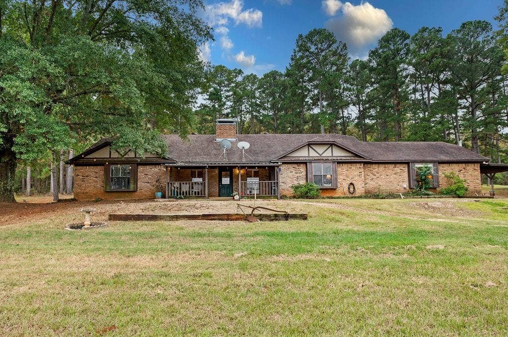 19418 CR 4125, Lindale, TX 75771 Ranch-style home featuring a porch, brick siding, a front lawn, view of scattered trees, and a chimney