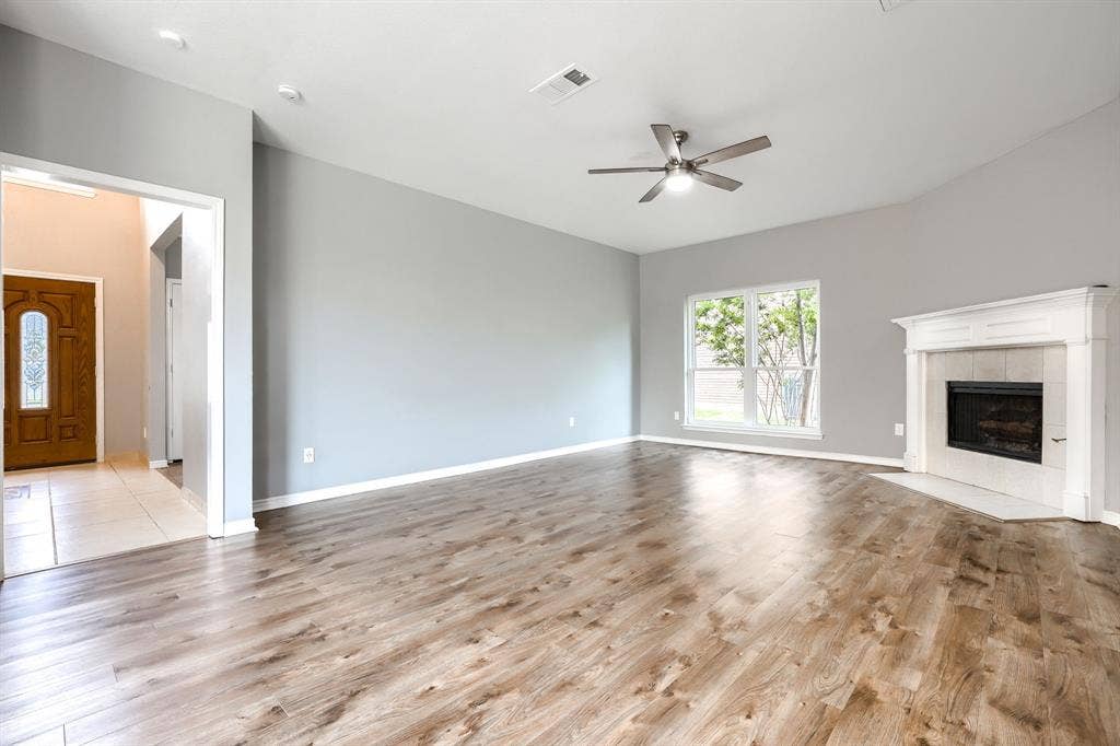 2309 York Court, Carrollton, TX 75006 Spacious living area featuring high vaulted ceilings, wood-finish flooring, a white mantel fireplace with tile surround, and a ceiling fan with integrated lighting