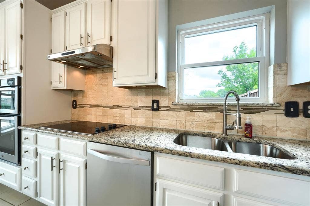 2309 York Court, Carrollton, TX 75006 Kitchen featuring white cabinetry, granite countertops, a stainless steel double sink with a gooseneck faucet, an electric cooktop, and a mosaic tile backsplash