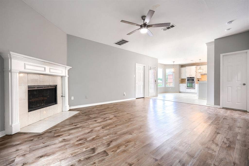 2309 York Court, Carrollton, TX 75006 Spacious living area featuring wood-finish flooring, a white mantel fireplace with tile surround, and vaulted ceilings with a ceiling fan