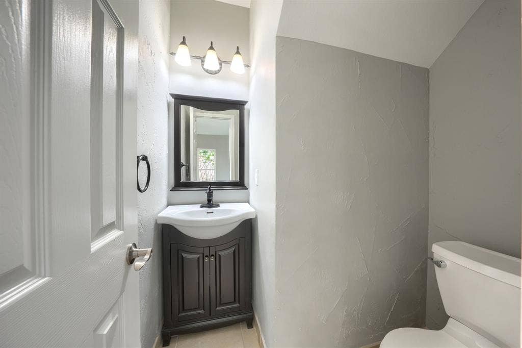 2309 York Court, Carrollton, TX 75006 Powder room featuring a dark wood-finish vanity with an integrated white sink, a framed mirror, and a three-light vanity fixture