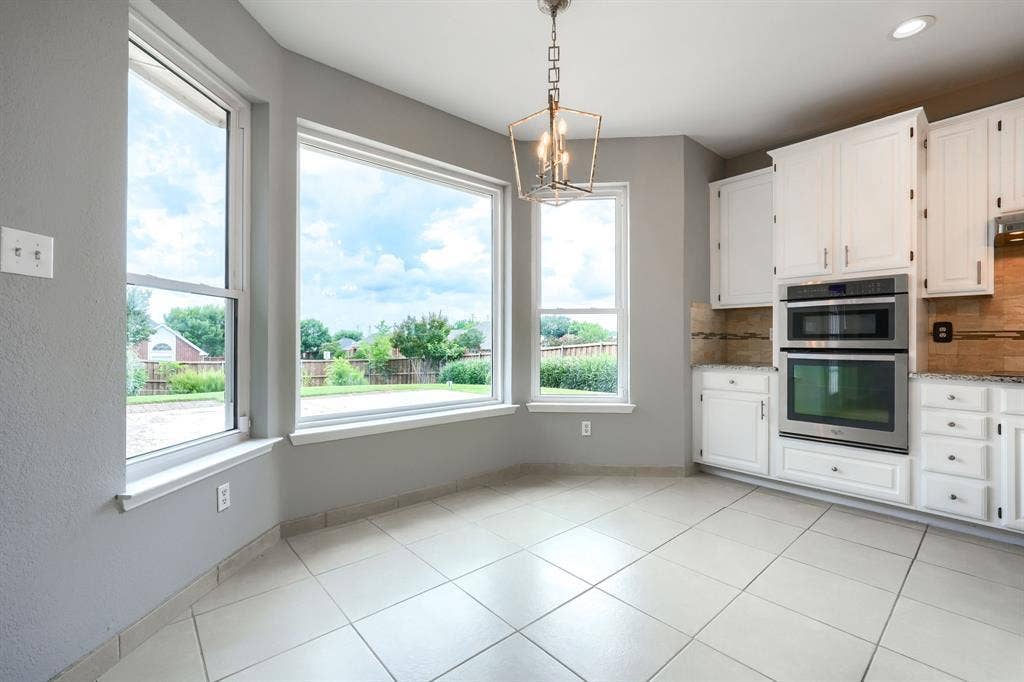2309 York Court, Carrollton, TX 75006 Kitchen dining area featuring white cabinetry, light-toned tiled flooring, stainless steel double ovens, granite countertops, and a decorative pendant light fixture