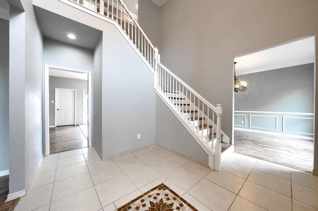 2309 York Court, Carrollton, TX 75006 Grand foyer featuring a white baluster staircase and light-toned tile flooring with a decorative mosaic inlay