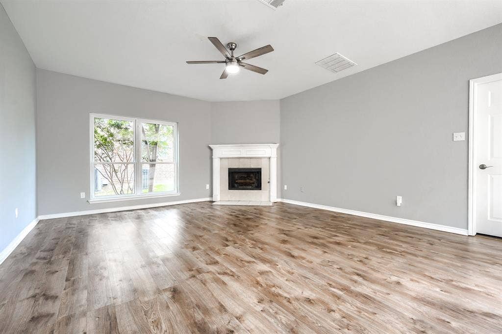 2309 York Court, Carrollton, TX 75006 Spacious room featuring wood-finish flooring, a corner fireplace with a white mantel, and a ceiling fan