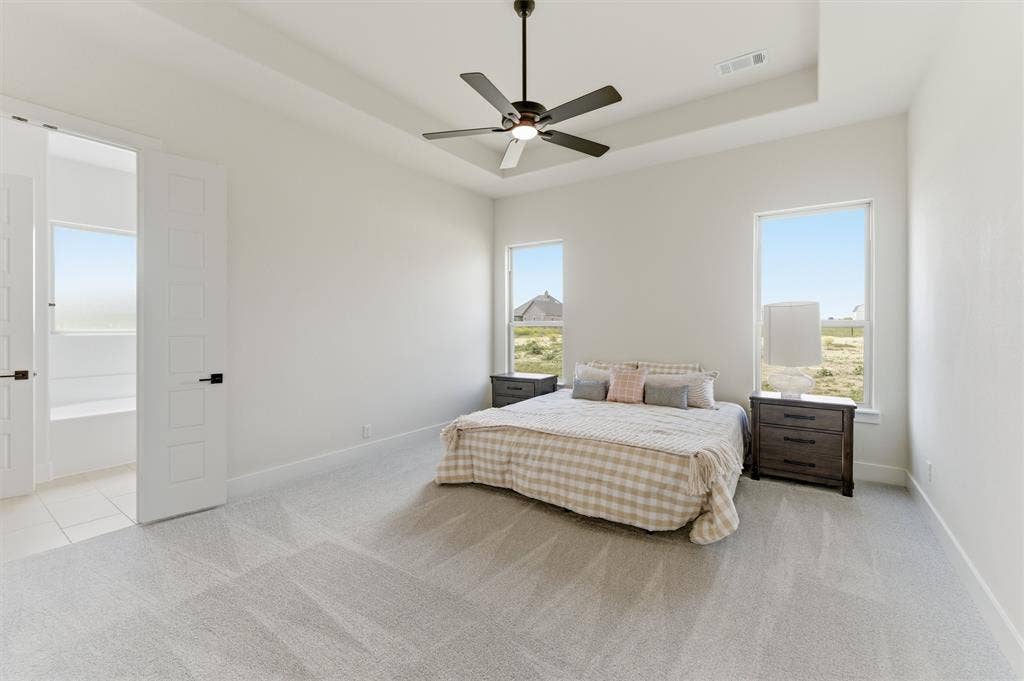 Spacious room featuring light gray carpet flooring, a tray ceiling with a black ceiling fan, and two large windows