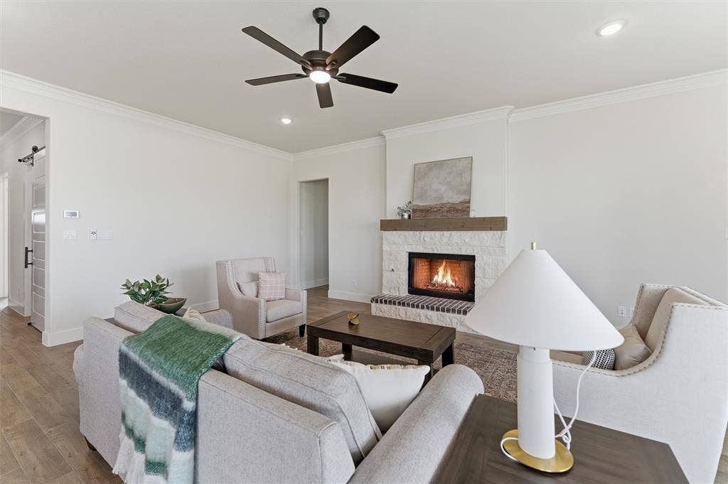 Living area featuring a stone-clad fireplace with a wood mantel, wood-finish flooring, recessed lighting, crown molding, and a ceiling fan
