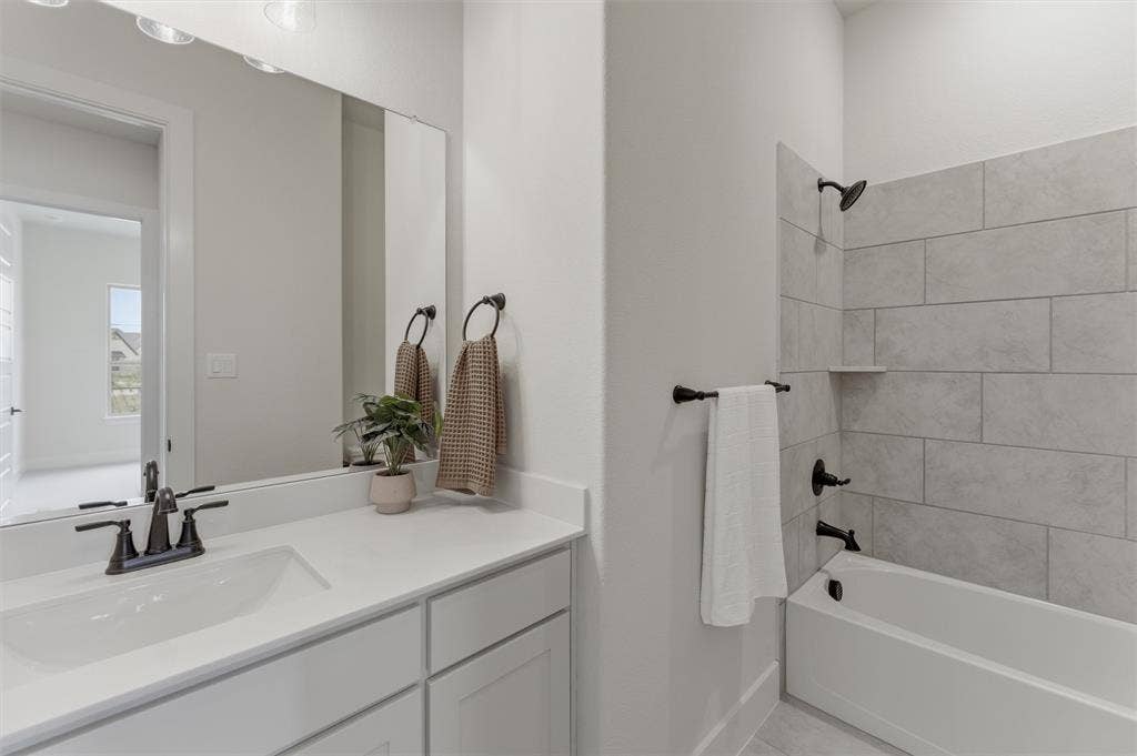 Bathroom featuring a single vanity with a white countertop and integrated sink, matte black faucet, and a shower-tub combination with light grey tile surround
