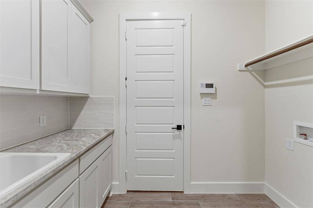 Laundry area featuring white cabinetry, a single basin sink, light grey countertop, and a white subway tile backsplash