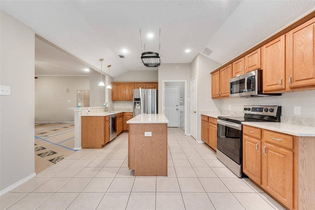 617 Madeline Court, Azle, TX 76020 Kitchen with stainless steel appliances, a center island, decorative light fixtures, vaulted ceiling, and light tile patterned floors