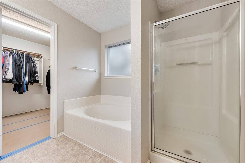 617 Madeline Court, Azle, TX 76020 Full bathroom featuring a spacious closet, a textured ceiling, a shower stall, and a garden tub