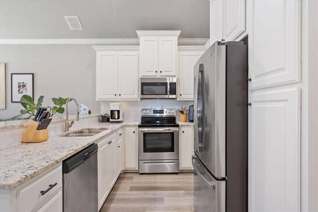 518 Alamo Court, McGregor, TX 76657 Kitchen featuring stainless steel appliances, light stone counters, white cabinets, crown molding, and light wood finished floors