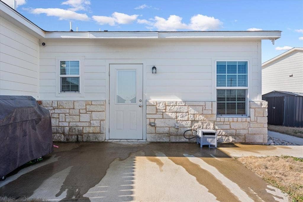 518 Alamo Court, McGregor, TX 76657 View of exterior entry featuring stone siding and a patio area