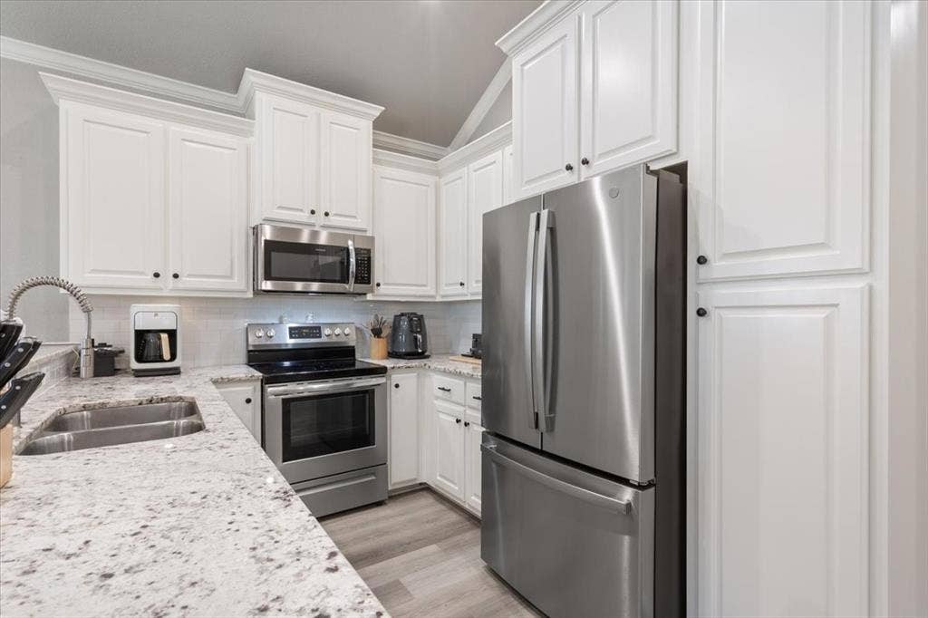 518 Alamo Court, McGregor, TX 76657 Kitchen with appliances with stainless steel finishes, light stone countertops, white cabinetry, vaulted ceiling, and backsplash