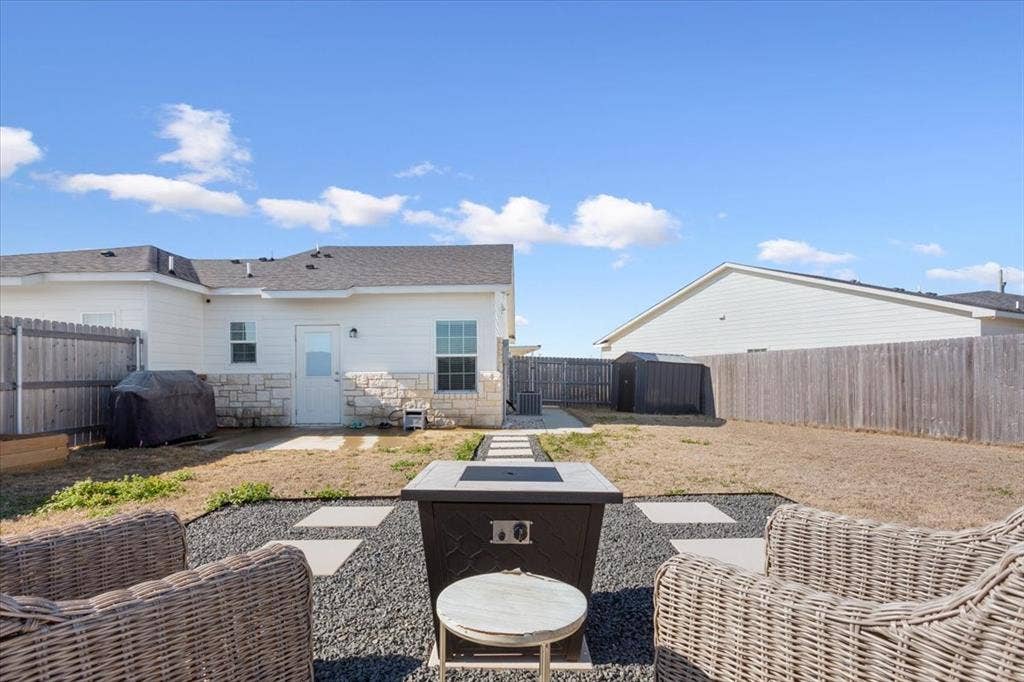 518 Alamo Court, McGregor, TX 76657 Rear view of property with a patio area, stone siding, a fenced backyard, an outdoor fire pit, and a shingled roof