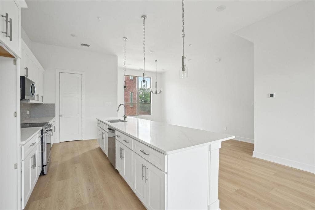 2524 Havenhurst Street, #102, Farmers Branch, TX 75234 Kitchen with white cabinets, stainless steel appliances, light wood-style floors, an island with sink, and pendant lighting