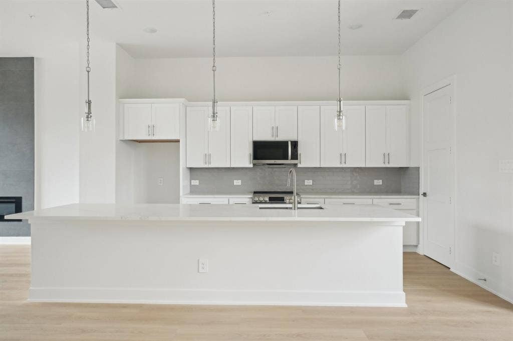 2524 Havenhurst Street, #102, Farmers Branch, TX 75234 Kitchen with decorative light fixtures, white cabinetry, light wood-type flooring, a large island with sink, and stainless steel appliances